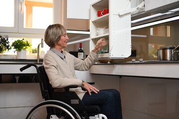 Eine Rollstuhlfahrerin nutzt die absenkbaren Systeme, um an Geschirr in den Oberschränken der Küche zu kommen. 