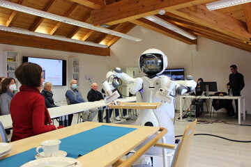 Eine Präsentation im Rahmen des Tag der offenen Tür im Projekt aus dem Forschungszentrum Geriatronik: Der Service-Humanoide GARMI trägt mit seinen Roboterarmen ein Tablett zu einem Esstisch, an dem eine Frau wartet. Er bringt ihr das Mittagessen.